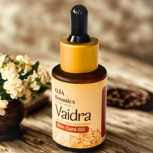 OJA Botanics Vaidra Skin Care Oil bottle on a wooden surface with flowers in the background