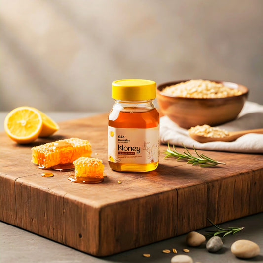 Jar of OJA BOTANICS honey on a wooden cutting board with lemon, honeycomb, and bowl in the background.